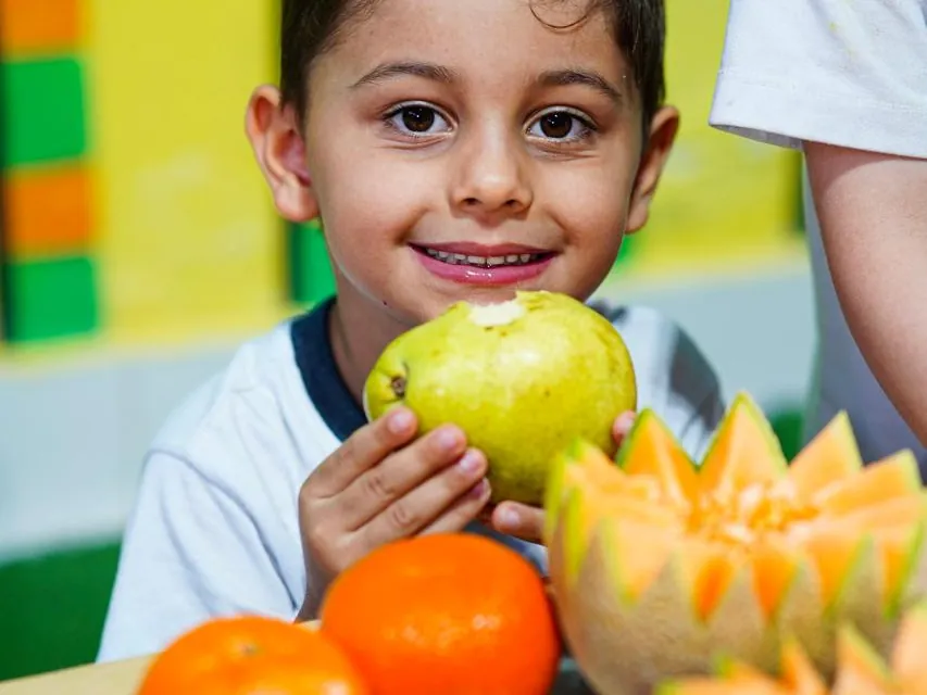 Menino com uma pera e uma mesa de frutas